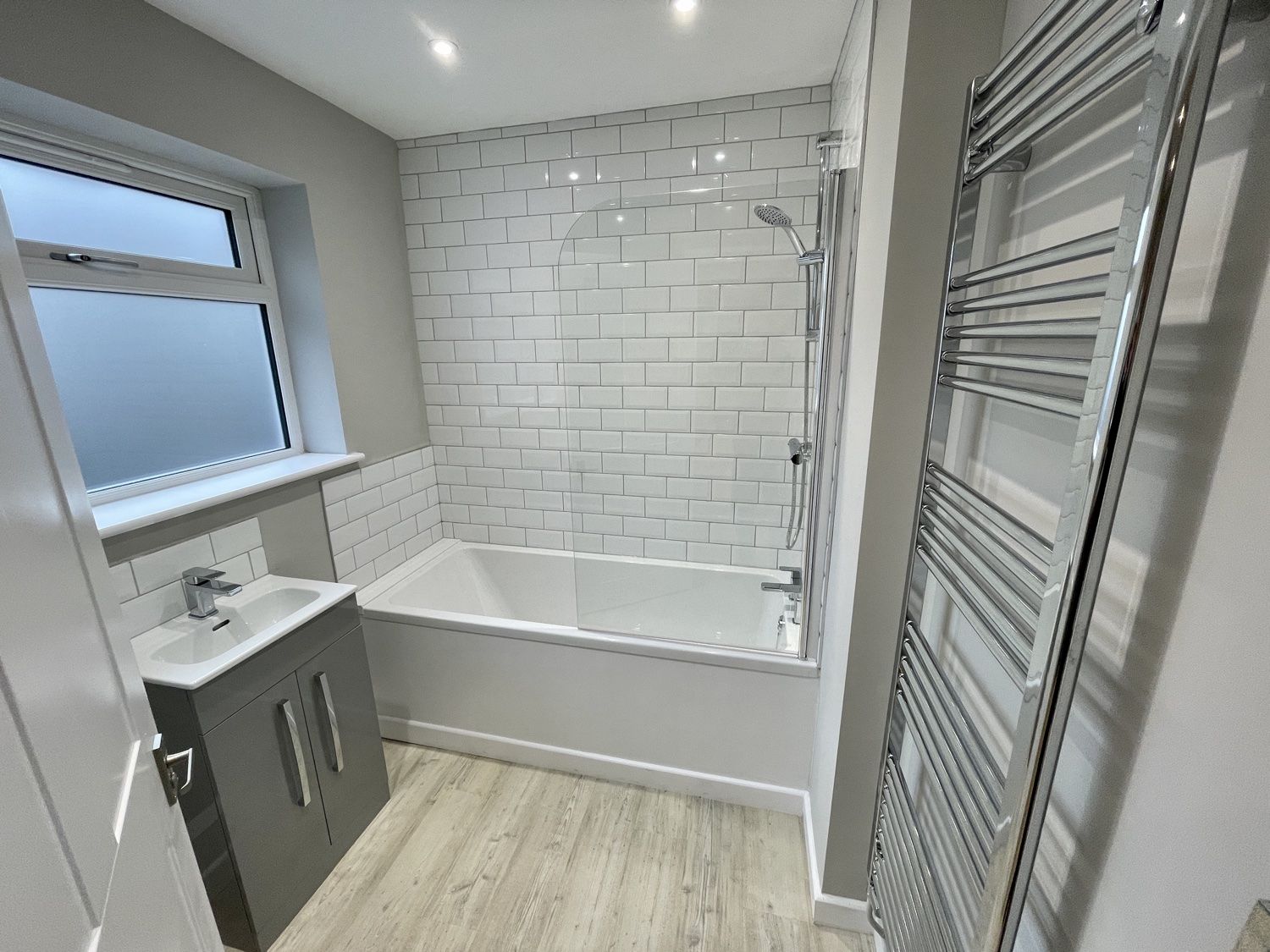 Bathroom after a complete refit: bath with metro tiles, shower screen, vanity basin and chrome towel rail