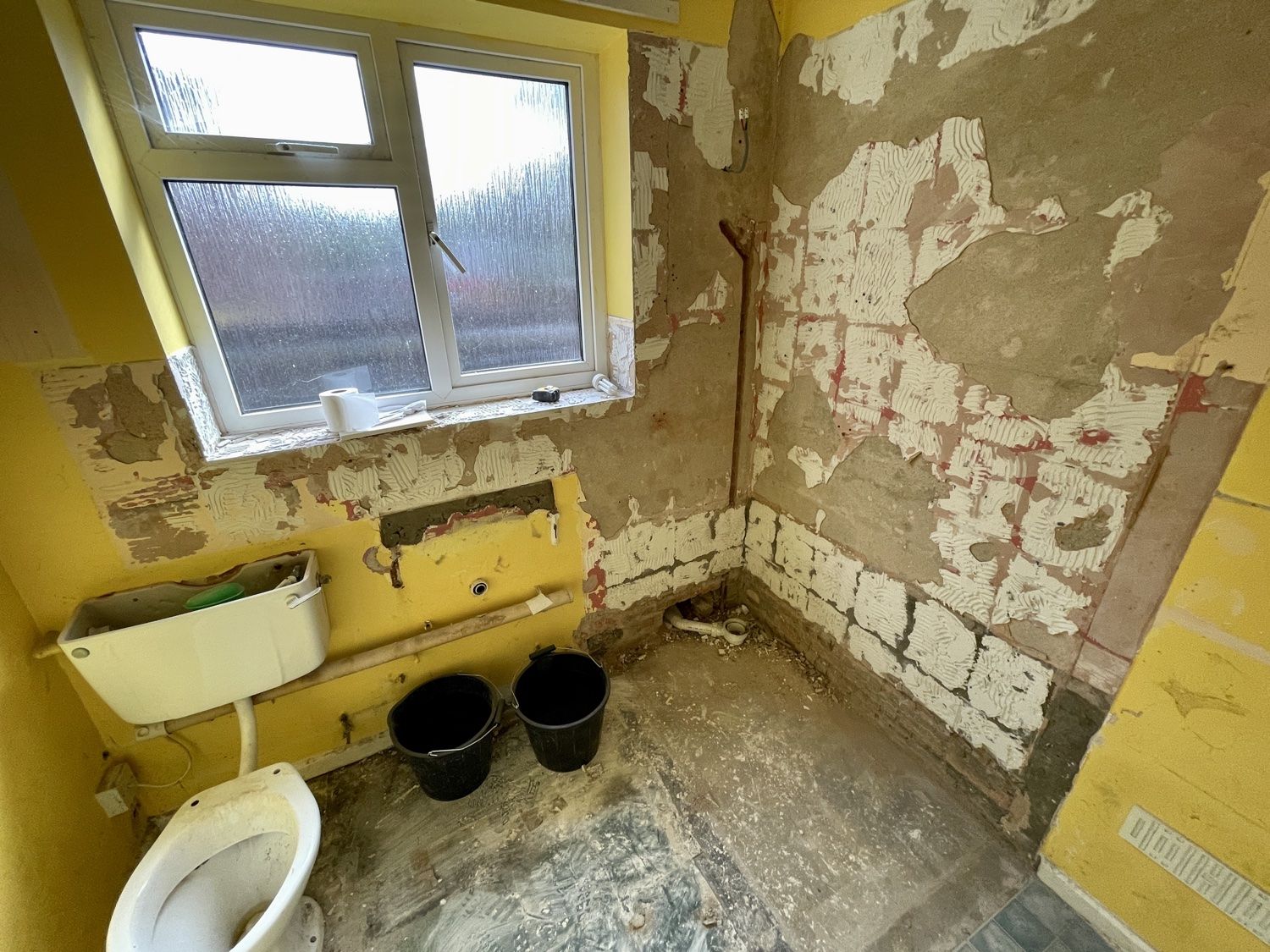 Bathroom before the refit: stripped room with yellow walls and the old toilet