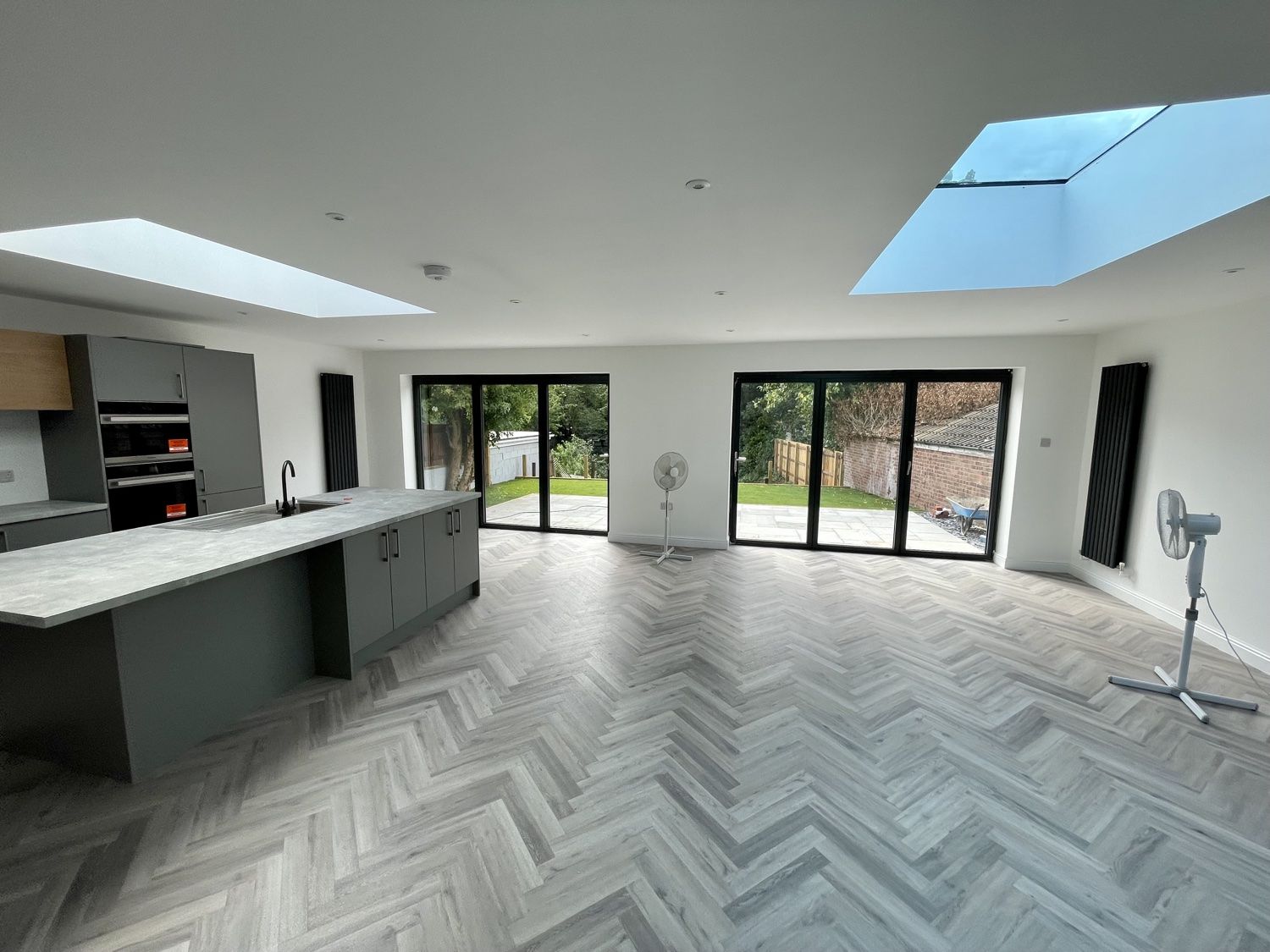 Open-plan kitchen and living area with herringbone floor, roof lights and bifold doors