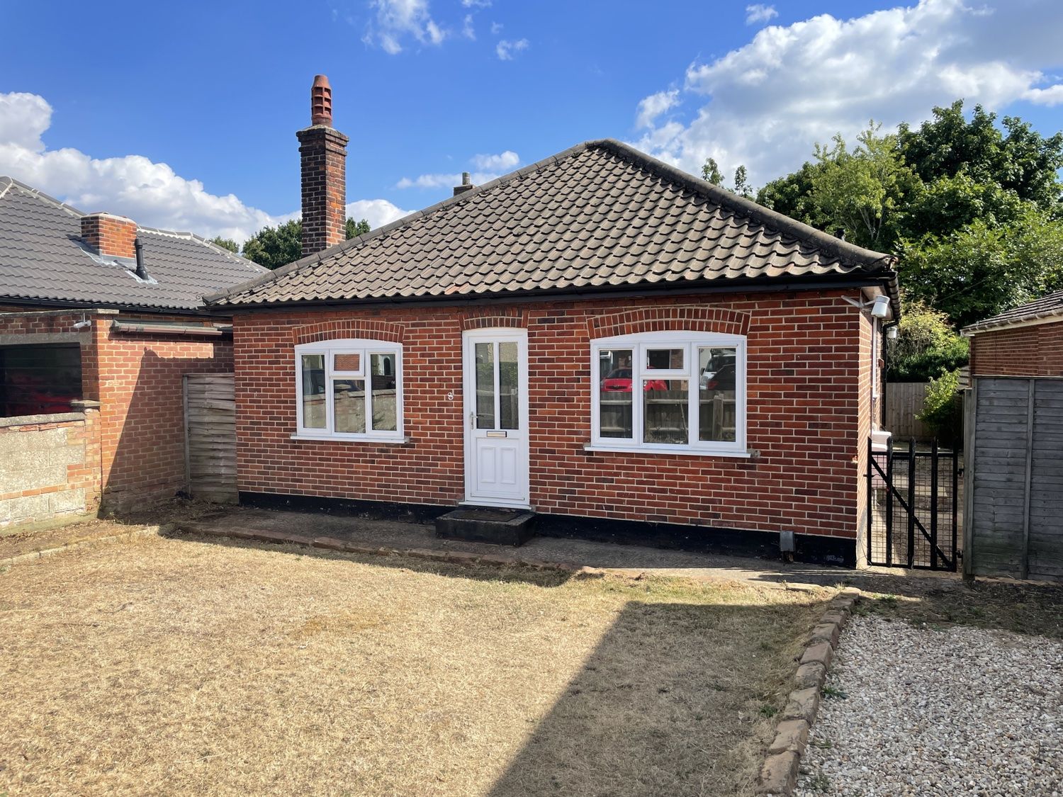 Bungalow before refurbishment: red brick, white windows and door, dry lawn